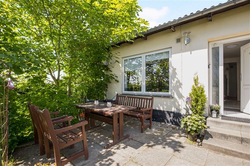 Træbord og stole i en have med en hvid dør og vindue i baggrunden