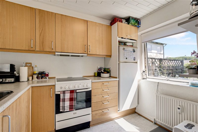 En lyse og moderne køkken med en hvid ovn og en række træskabe, der er udstyret med håndtag og hylder