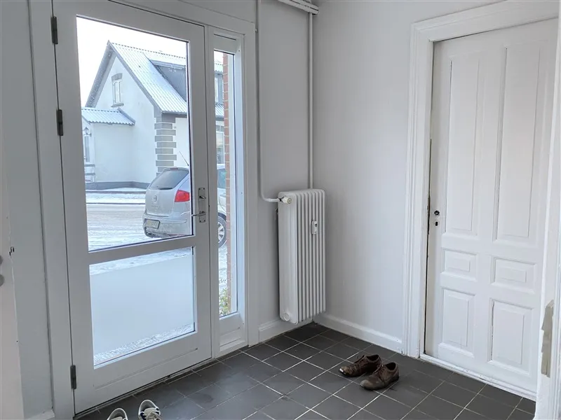 En indgangsdør med sko og radiatorer, hvor der står en bil parkeret udenfor i sneen