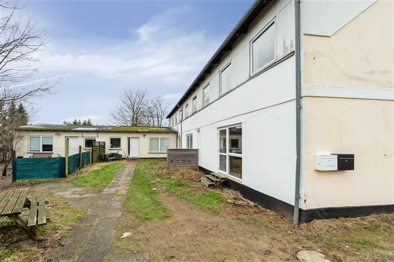 Et hus med grønne ruder og en veranda uden for. En grøn gitterhegnet er på den ene side. Et træbord uden for hus.