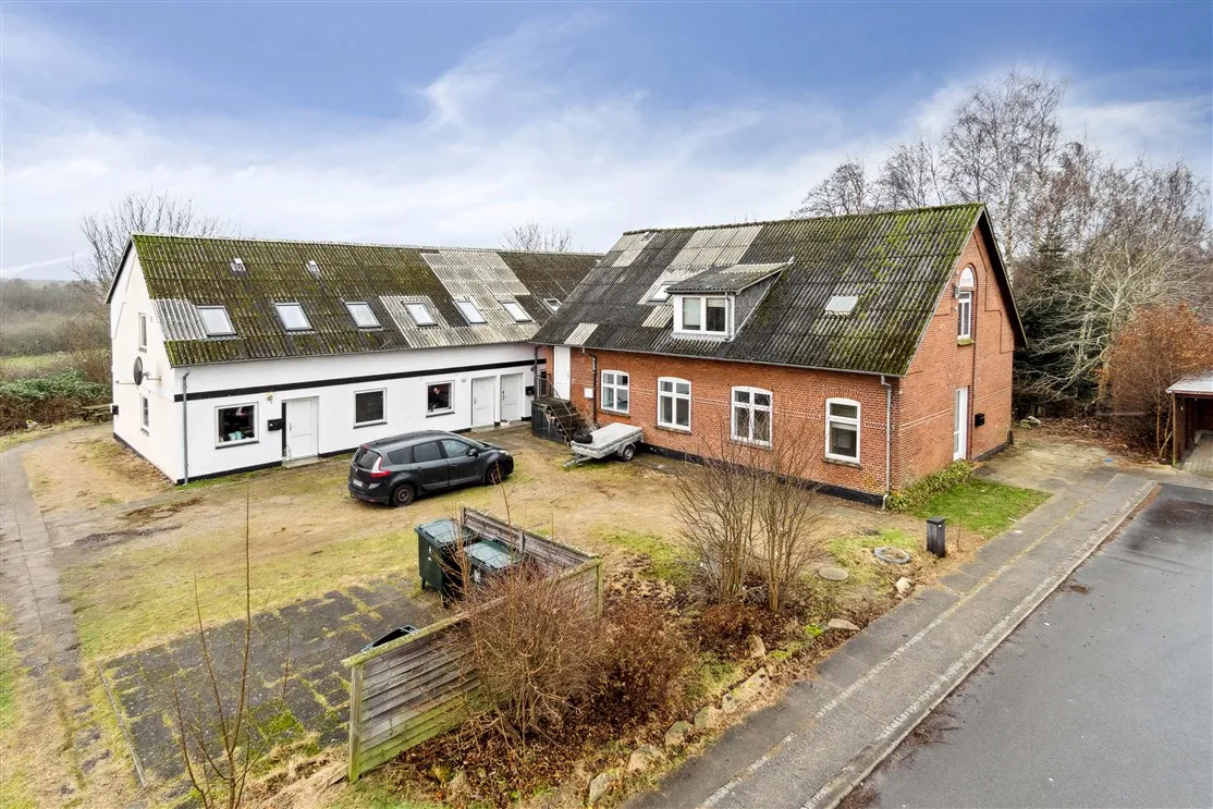 Store røde og hvide bygninger med garage og parkeringsplads. Børnehave, skole, butik og strand i nærheden.