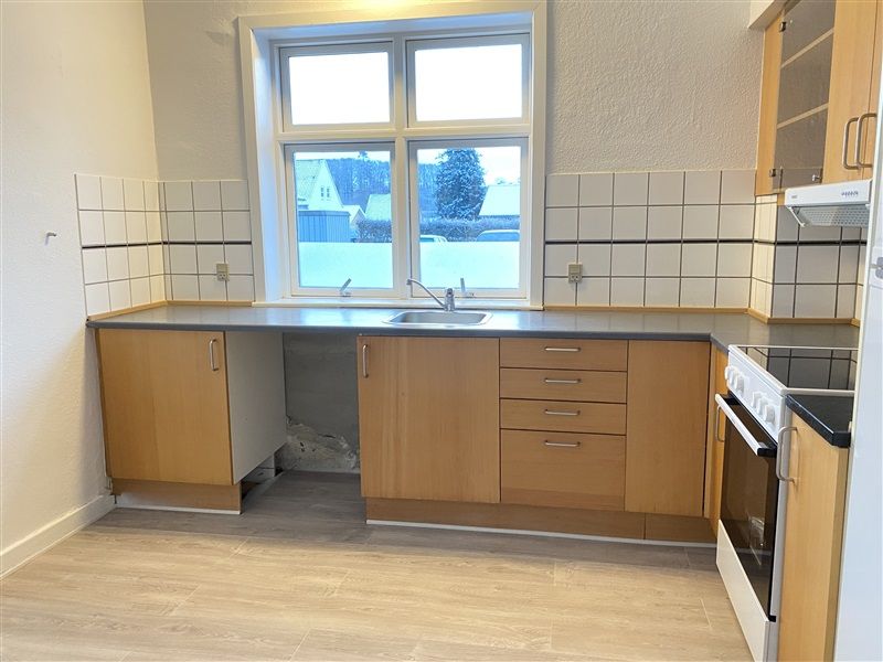 Rent køkken med lyse, lysegrå vægge og gulve samt lyse, møblerede hængeskabe og bordplade