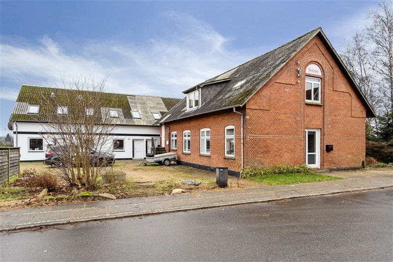 To huse i røde mursten med skifertag og hvide ruder samt en trailer og en skraldspand på forsiden