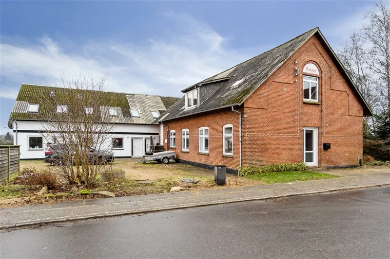 To huse i røde mursten med skifertag og hvide ruder samt en trailer og en skraldspand på forsiden