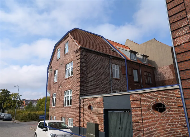 Bred røde murstensbygning med tagrenne og to runde vinduer og højt skrånende tag