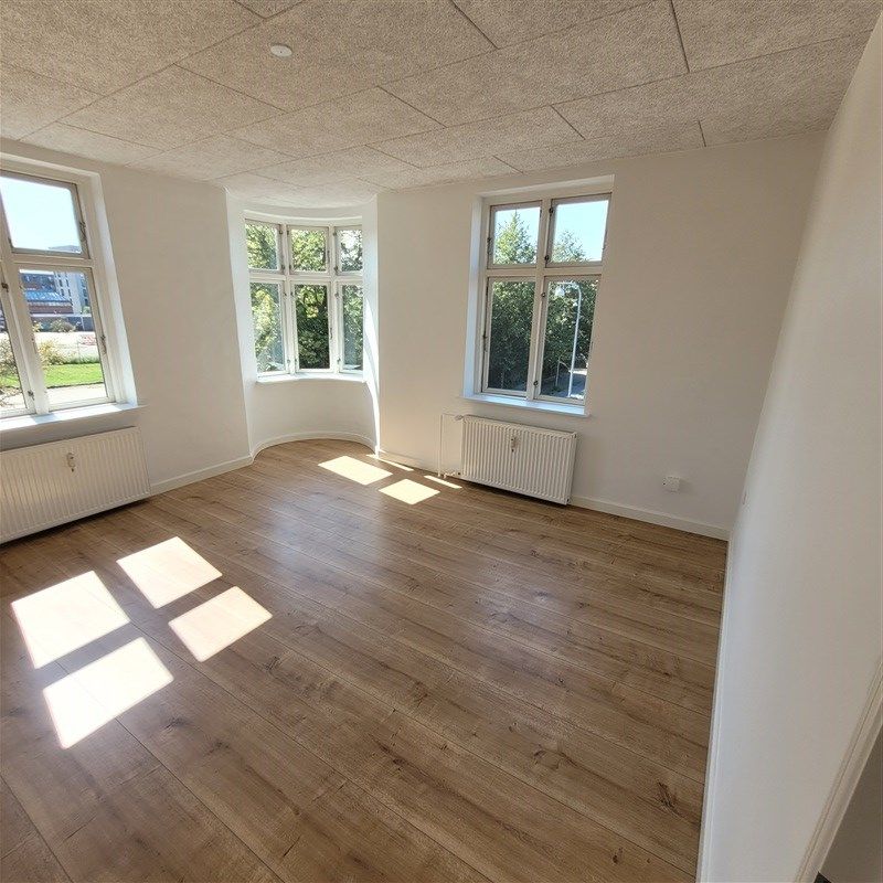 Indvendørs værelser med lyse gulve og store ruder i hvide vægge, træruder og hvide radiatorer