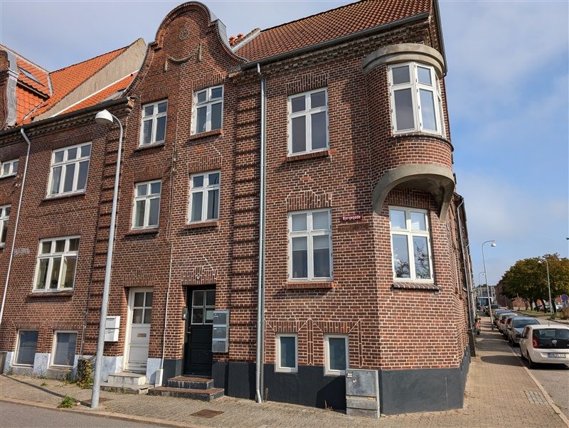 Smukt renoveret bygning med røde mursten og flere vinduer på hjørne i Bjergegade