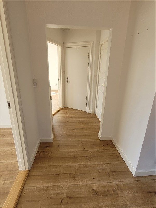 Renoveret gang med hårdt trægulv og hvide vægge samt lyse døre og lyse gulvbelægning