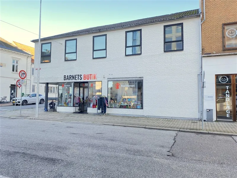 Barnets Butik på Danmarksgade 21A i Fredericia med skiltet og Red Barnet logo i vinduet og tøj udenfor