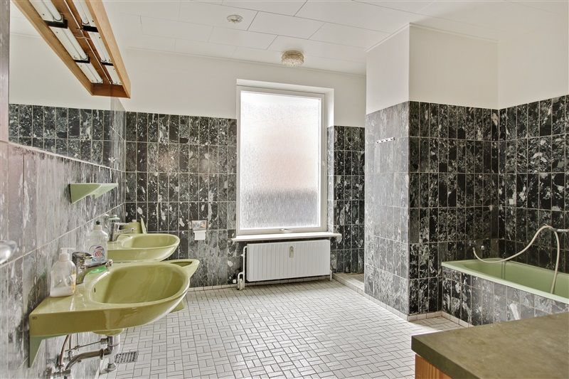 Foto af et badeværelse med to lyse grønne vasker og et badekar med vandhane. Murene er klædt i mørke og lyse grønne