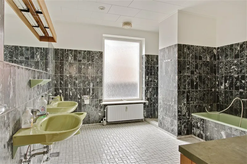 Foto af et badeværelse med to lyse grønne vasker og et badekar med vandhane. Murene er klædt i mørke og lyse grønne