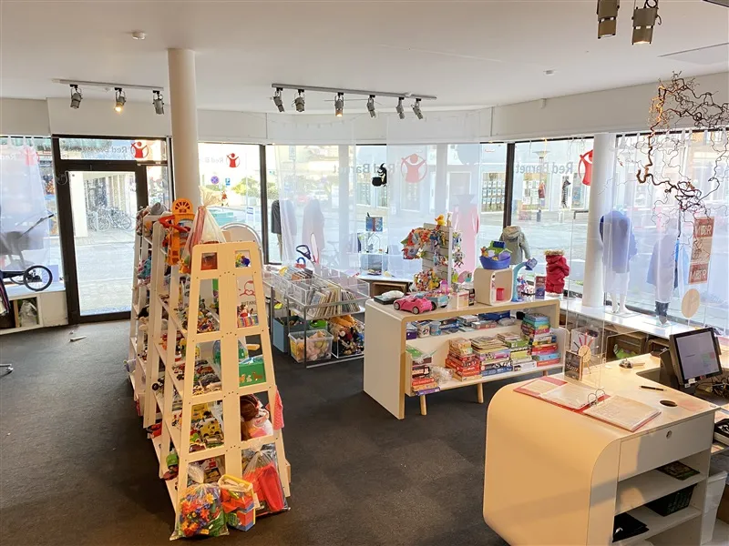 Et indre af et nyt butikslokal med hylder, skuffer, og udstille varer som bøger, legetøj, og pynt. Foran er et gulv med