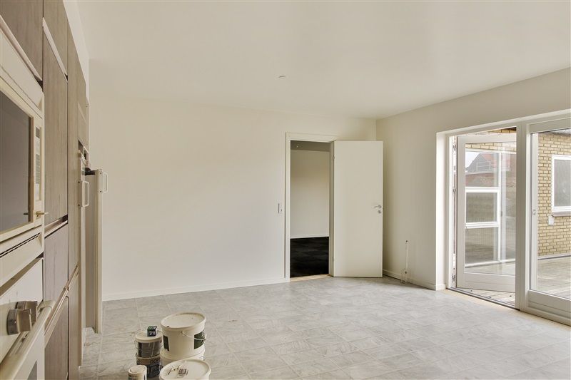 Et tomt værelse med åbne døre, tomme malingsspand og en hvidgulv samt hvide vægge