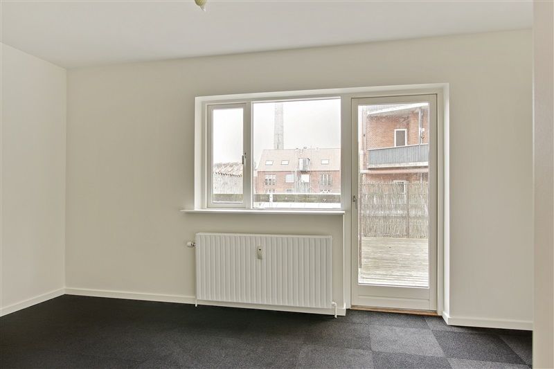 Foto af en møbleret lejlighed med lyse vægge og tæppegulv, et glasdørsystem og et hvidt radiator