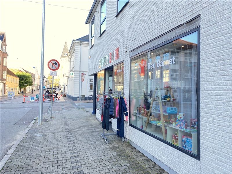 En butik med navnet Red Barnet og en klædeskab med forskellige farvede tøj på hængestikker foran butikken og en