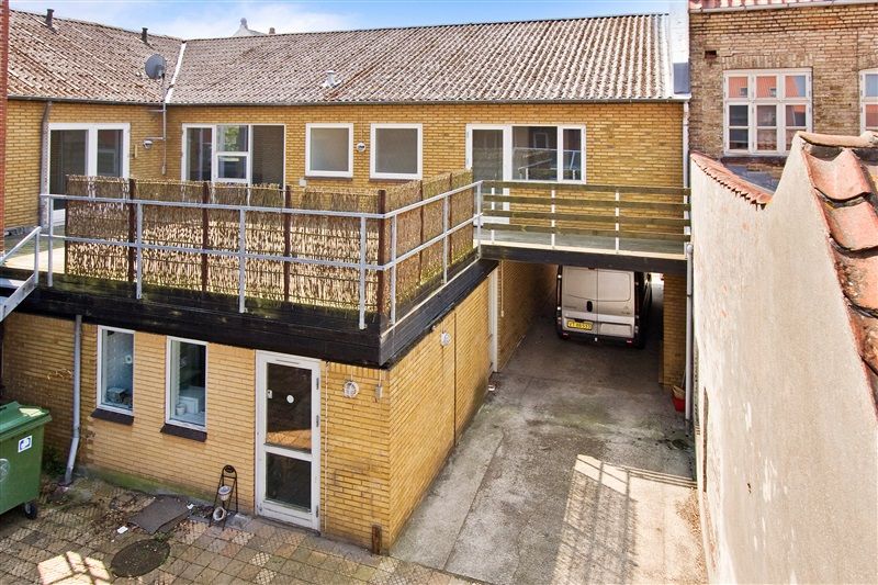 Nydelivets udlejningsejendom på Danmarksgade 21A med en terrasse, garage og grøn affaldscontainer.