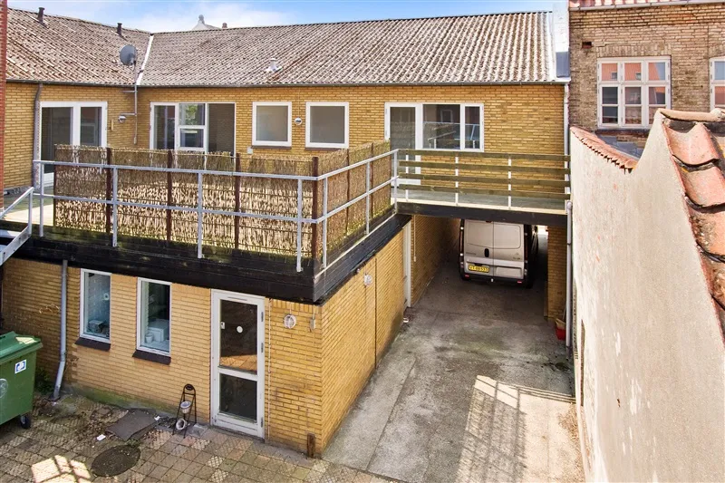 Nydelivets udlejningsejendom på Danmarksgade 21A med en terrasse, garage og grøn affaldscontainer.