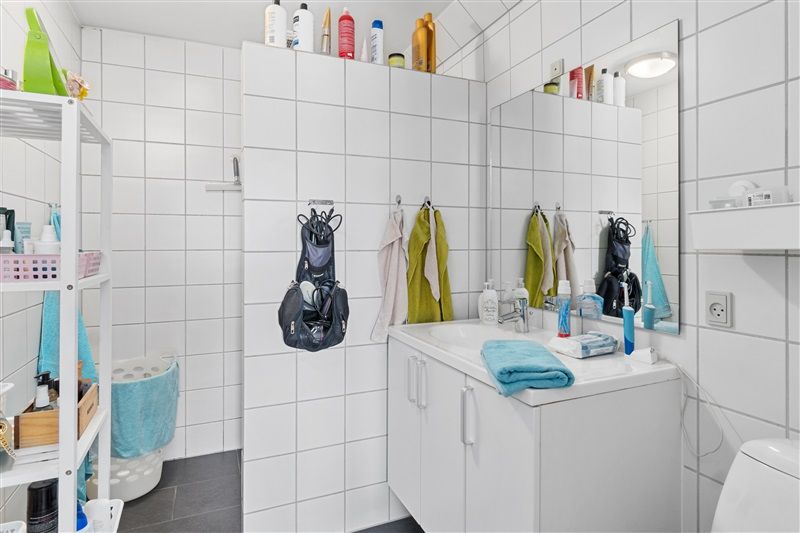 Ren designet badeværelse med hvide kakel, toilet, hængende håndklæder, hvidt toilet, vask med spejl, hængende