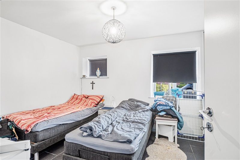 To soveværelser med hver deres seng og to vindu med gardiner og en lysarmatur på loftet