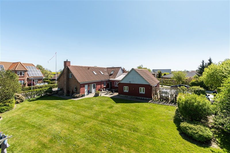 Tre røde og hvide huse med solceller på taget og udsigt over en stor grøn græsplæne