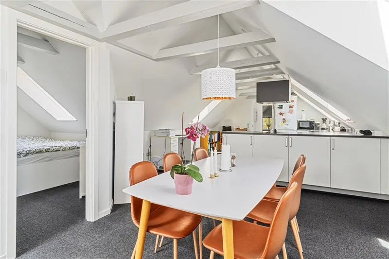 Værelse med loftsværelse, hvidt bord og stolen, køkken med hvide skabe og mikroovn, gulv med grønne mønstre og lysekroner