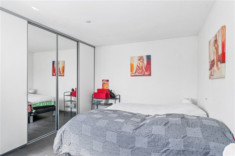 Indenfor et soveværelse er der et stort dobbeltseng med et mønstret dynelag og et glasregn. I enden af værelset er der en