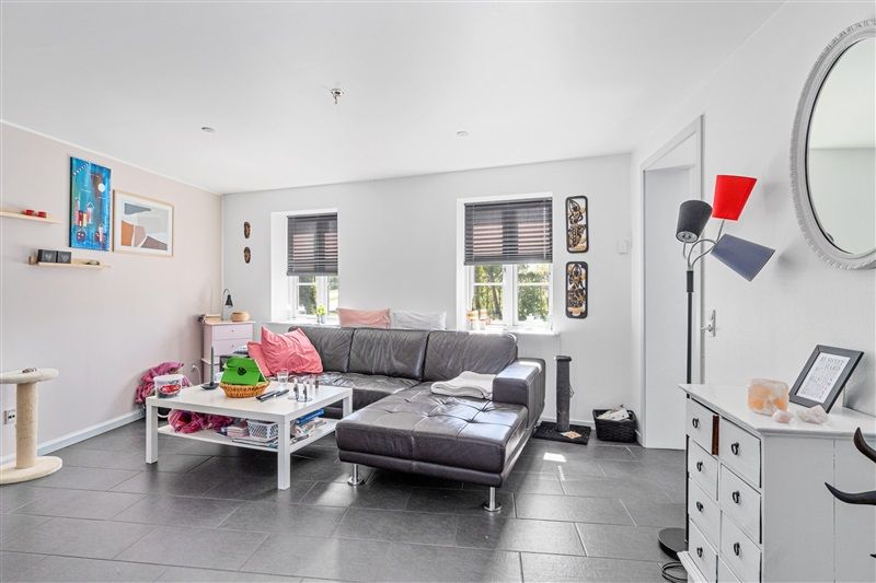 Nydelig stue med hvid væg og sort gulv. Sort lædersofa med hvidt bord og kaffebord med diverse genstande. Væg med