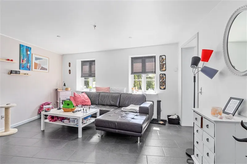 Nydelig stue med hvid væg og sort gulv. Sort lædersofa med hvidt bord og kaffebord med diverse genstande. Væg med