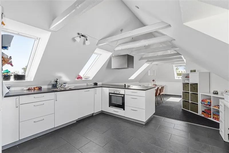 Lejlighed i 1. sal med højloft og loftsvinduer, hvide køkkenskabe, sort bordplade og en integreret ovn