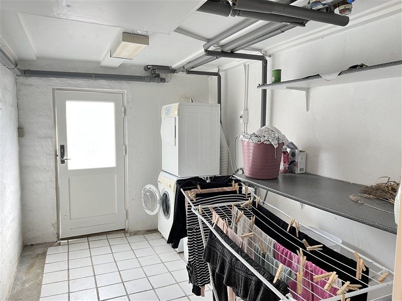 Moderne vaskerum med hvidt loft og vægge. Hvidt gulv med højkvalitets fliser. Hvide vaskemaskine og tørretumbler. Pink