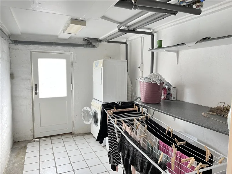 Moderne vaskerum med hvidt loft og vægge. Hvidt gulv med højkvalitets fliser. Hvide vaskemaskine og tørretumbler. Pink