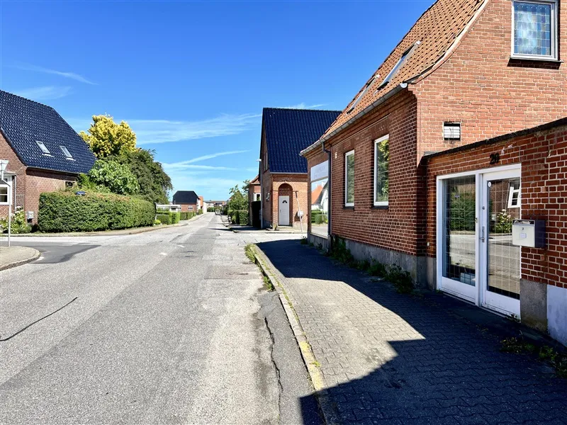 Vej med to sider, begge med huse og buske og to huse med røde mursten og vinduer med hvide indfatninger