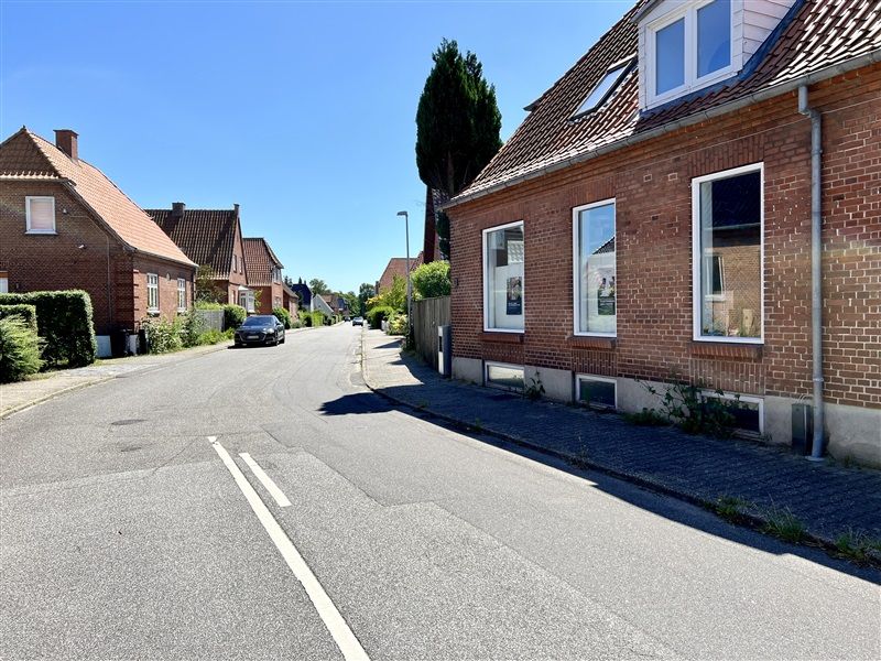 Bred gadegade med en bil, der kører mod venstre, og et hus med tre vinduer i første række