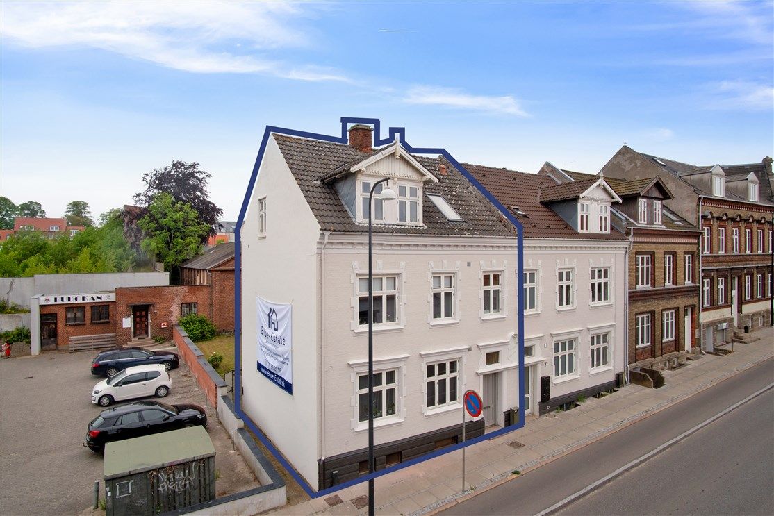 Sjællandsgade 5 i Fredericia med renoveret og optimeret udlejningsejendom, reklamebanner og biler parkeret foran