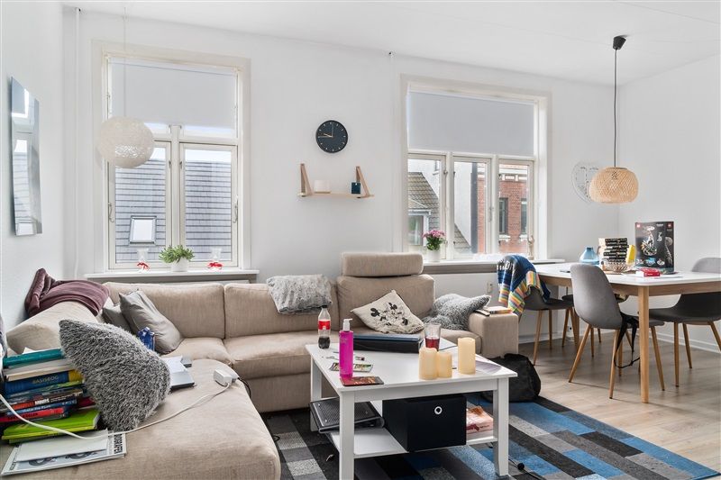 Værelse med høj loftshøjde og to store vinduer med persienner. Møbler inkluderer sofa, bord og stole samt skrivebord og