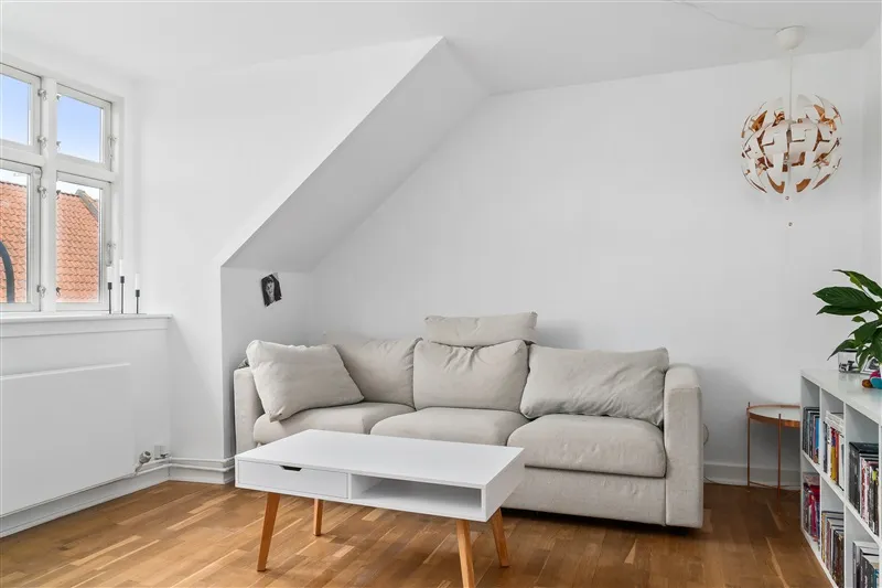 Et moderne og rent værelse med hvidt loft, hvid sofa, højt vindue og moderne møbler samt lysegul gulvbelægning