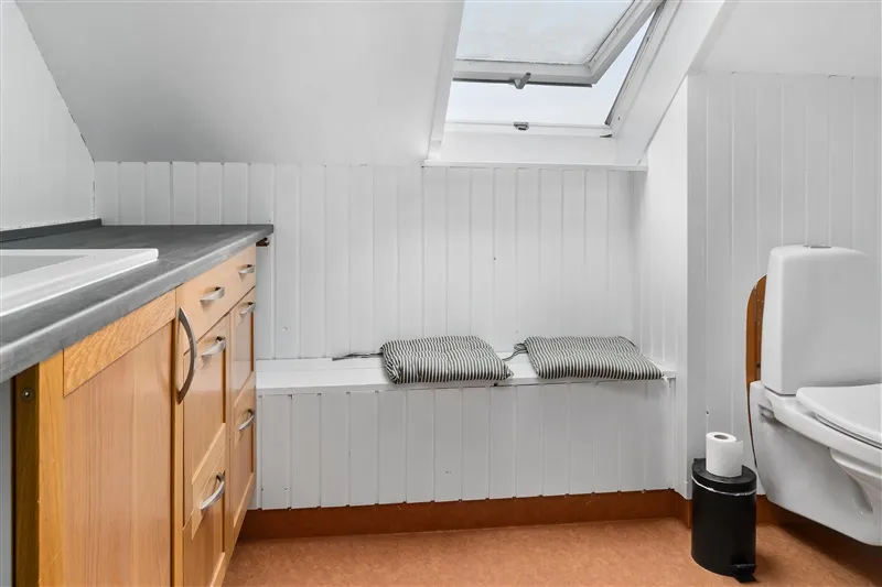 Rent og minimalistisk badeværelse med hvidt loft og vægge, lysegråt bordplad og tre træskuffer