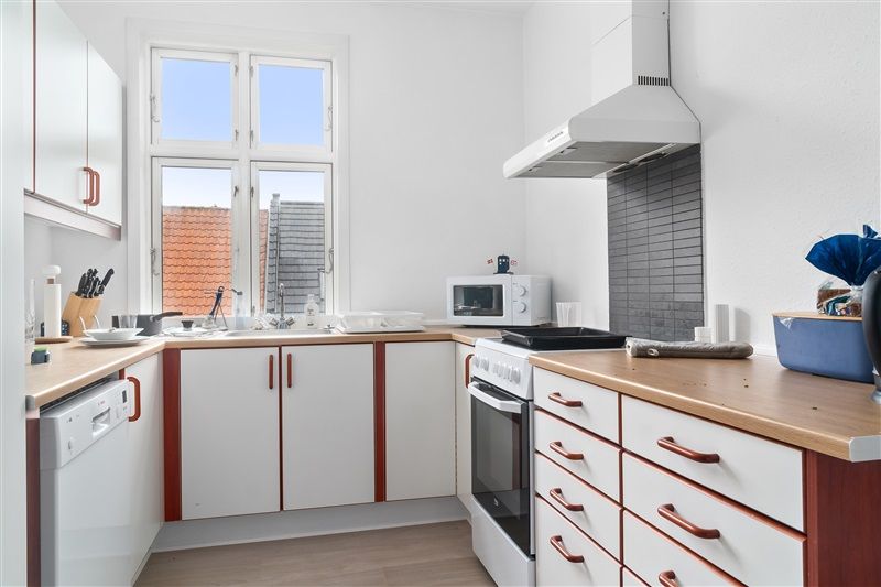 Rent og pænt køkken med hvide skabe og træbordplade samt ovn og mikroovn