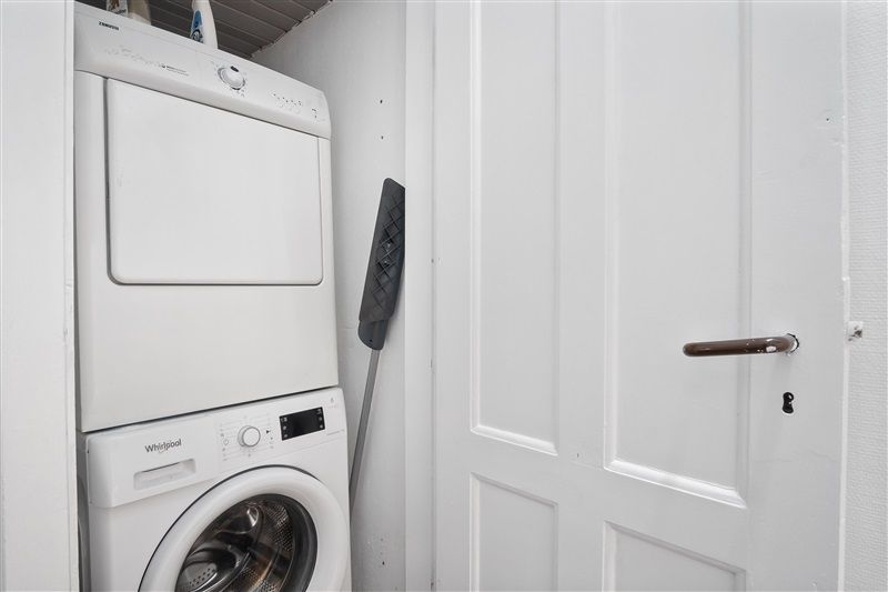 På et hvidt værelse med en hvid dør og hvide vægge står et hvidt tøjvaskeri og en hvid tørretumbler placeret sammen