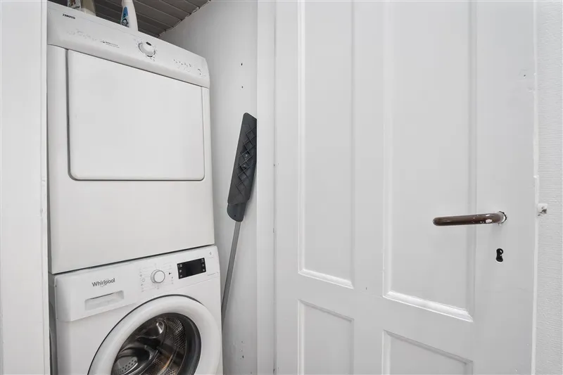 På et hvidt værelse med en hvid dør og hvide vægge står et hvidt tøjvaskeri og en hvid tørretumbler placeret sammen