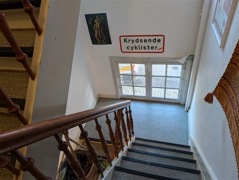 Tre trin med håndtag og krydsende cykelstierskilt på væggen med skrånende loft og vinduesglas