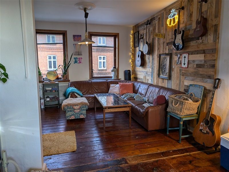 Soveværelse med møbleret sofa og skrivebord, lyse pletter på gulvet og musikinstrumenter og indretning