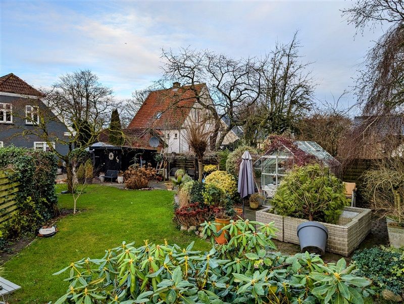 Have med grøn græsplæne og buske foran huse og træer i Frederikshavn