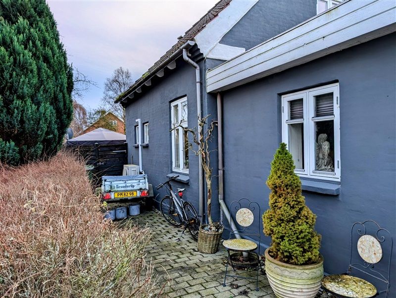 Havepladsvej 50, Fredericia med terrasse, snorcykel og træer med lyserøde blomster. Have med skulptur og to hængestole med