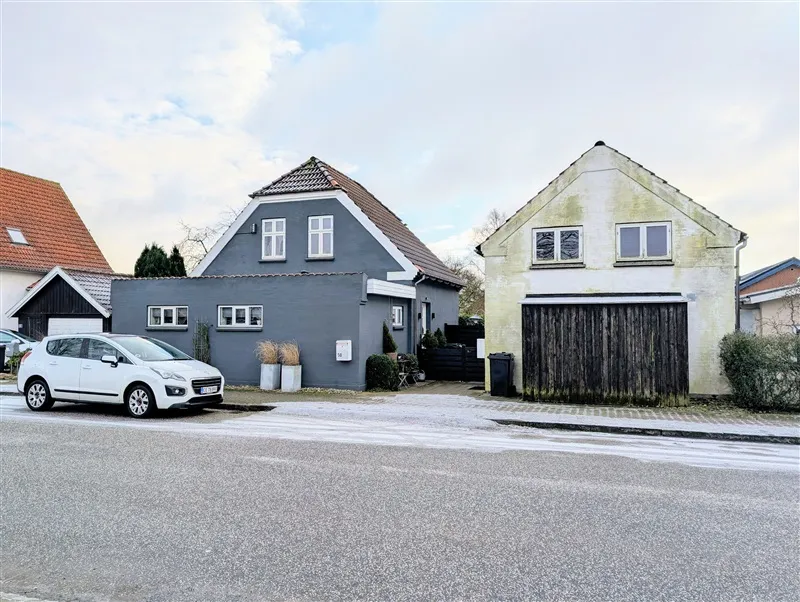 Huse med røde tag i kvarteret, hvor en hvid Peugeot 408 er parkeret og en række planter står foran