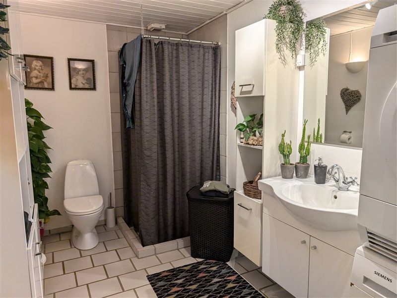 Rent og funktionelt badeværelse med hvid toilet, badeværelsesskabe og plante i hjørnet