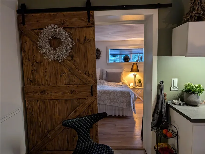 En køkken med et højt loft og en træskufledør med krans og en stol og en plante på en hylde