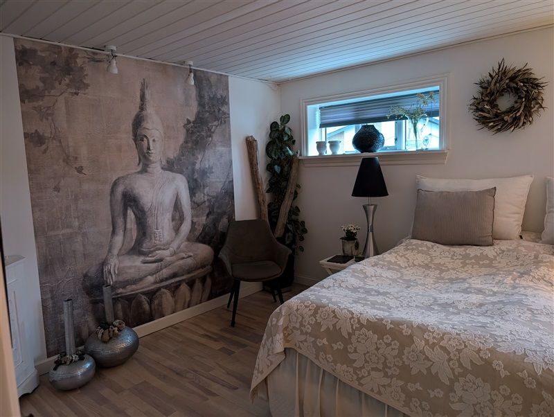 Hjemmets værelse med beige tæppe og hvid pude, Buddha maleri på væggen, lænestol og plante og lysestage på højbordet