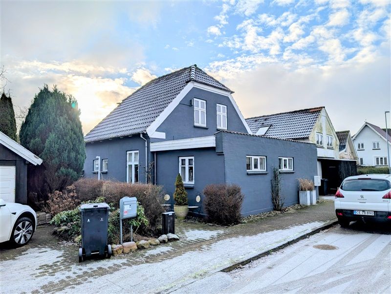 Købehus med stor have i Havepladsvej 50 i Fredericia. To biler parkeret foran og udsigt til solnedgang. Have med buske og