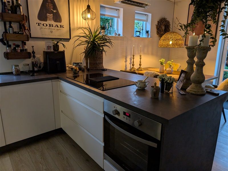 Køkken med en stor sort ø, en ovn, et bord med puder og et billede af Tobak på væggen